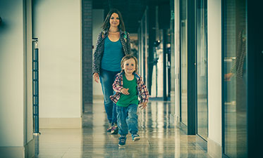 Vergrößerungsansichten für Bild: Foto: Ein Flur mit Bürotüren auf dem ein Kind vor seiner Mutter läuft