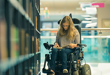 Frau in Rollstuhl in einer Bibliothek.