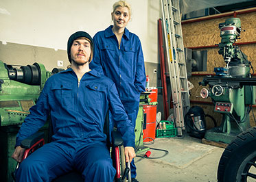 Vergrößerungsansichten für Bild: Ein Mann im Rollstuhl in einer Werkstatt, daneben steht eine Frau.