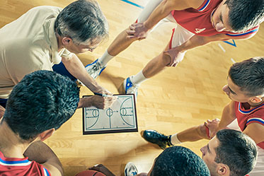 In der Sporthalle: Trainer mit Taktiktafel vor Spielergruppe