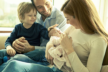 Gruppenfoto: Eine Familie sitzt zusammen: der Junge sitzt beim Vater auf dem Schoß und die Mutter hält das Baby im Arm.