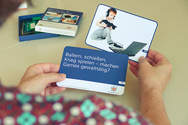 Nahaufnahme: Das Bild zeigt zwei Hände, die Karten zum Thema Videospiele und Gewalt in den Händen halten.
