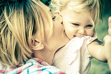 Nahaufnahme: Mutter hält ihr Kind auf den Arm und gibt ihm einen Kuss auf die Wange