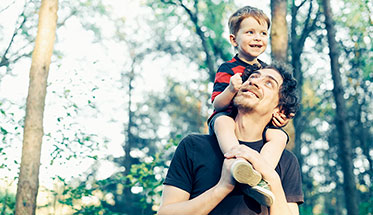 Foto: Ein Vater trägt ein Kind auf den Schultern beim Spaziergang im Freien.