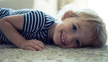 Ein Kleinkind liegt auf dem Boden und lacht in die Kamera.