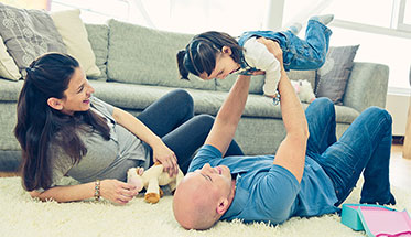 Vergrößerungsansichten für Bild: Foto: Eine Familie liegt auf dem Boden und der Vater hält die Tochter in die Luft