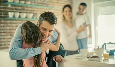 Vergrößerungsansichten für Bild: Nahaufnahme: Im Vordergrund verabschiedet sich ein Vater von seiner Tochter und im Hintergrund steht die Mutter mit dem Sohn im Arm