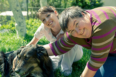 Szene im Garten: Eine ältere Frau und eine junge Frau streicheln einen Hund.