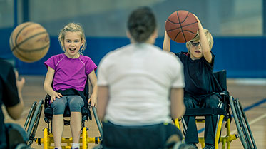 Vergrößerungsansichten für Bild: Kinder im Rollstuhl beim gemeinsamen Basketballspielen in der Turnhalle.
