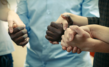 Nahaufnahme: Hände unterschiedlicher Hautfarben halten sich gegenseitig fest.