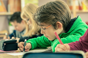 Vergrößerungsansichten für Bild: Nahaufnahme: Kinder sitzen schreibend an einem Tisch