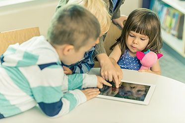 Vergrößerungsansichten für Bild: Nahaufnahme: Vier kleine Kinder schauen sich etwas auf einem Tablet an