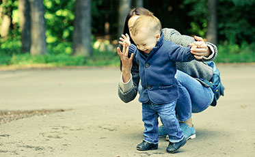 Vergrößerungsansichten für Bild: Foto: Kleines Kind macht Laufversuche und die Mutter sitzt helfend dahinter.