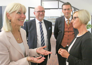 Staatssekretärin Carolina Trautner mit weiteren Personen lächelnd. 