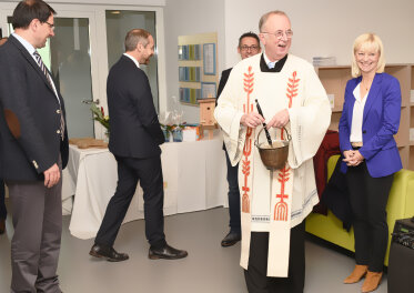 Staatssekretärin Carolina Trautner lächelnd hinter dem Geistlichen. 