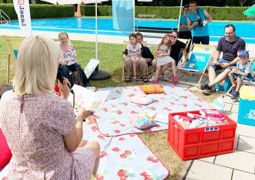 Staatssekretärin C. Trautner, auf Picknickdecke sitzend, liest Kindern vor