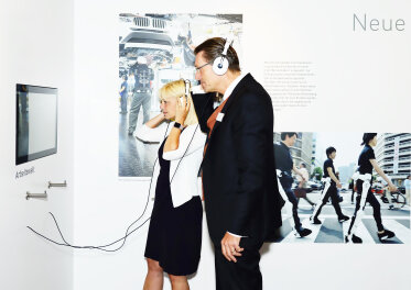 Staatssekretärin Carolina Trautner und Norbert Kollmer schauen in einen Bildschirm und haben Kopfhörer auf. 