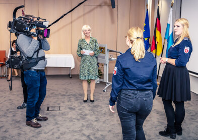 Auf dem Bild sind 4 Personen zu sehen. Staatsministerin Carolina Trautner unterhält sich mit zwei Preisträgerinnen. Dazu ein Kameramann. 