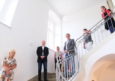Auf diesem Bild sind 6 Personen zu sehen, die auf einer Treppe verteilt stehen und in die Kamera sehen. 