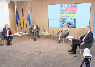 Staatsministerin Carolina Trautner sitzend in einem großen Sitzungsraum mit Bildschirmwand im HIntergrund