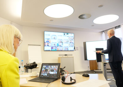 Sozialministerin Carolina Trautner vor einem Bildschirm auf der eine Videokonferenz stattfindet. 
