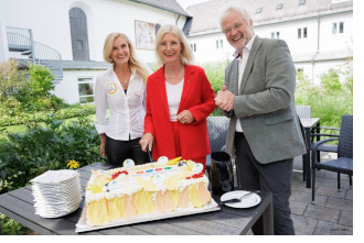 Das Foto zeigt eine Torte mit dem Signet 'Bayern Barrierefrei' und von links nach rechts: Jugendherbergsleiterin Ulrike Abeln der Jugendherberge Burghausen, Sozialministerin Ulrike Scharf und der Präsident des Deutschen Jugendherbergswerks Klaus Umbach