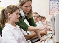 Lehrerin unterrichtet Schülerinnen und deutet auf Computermonitor.