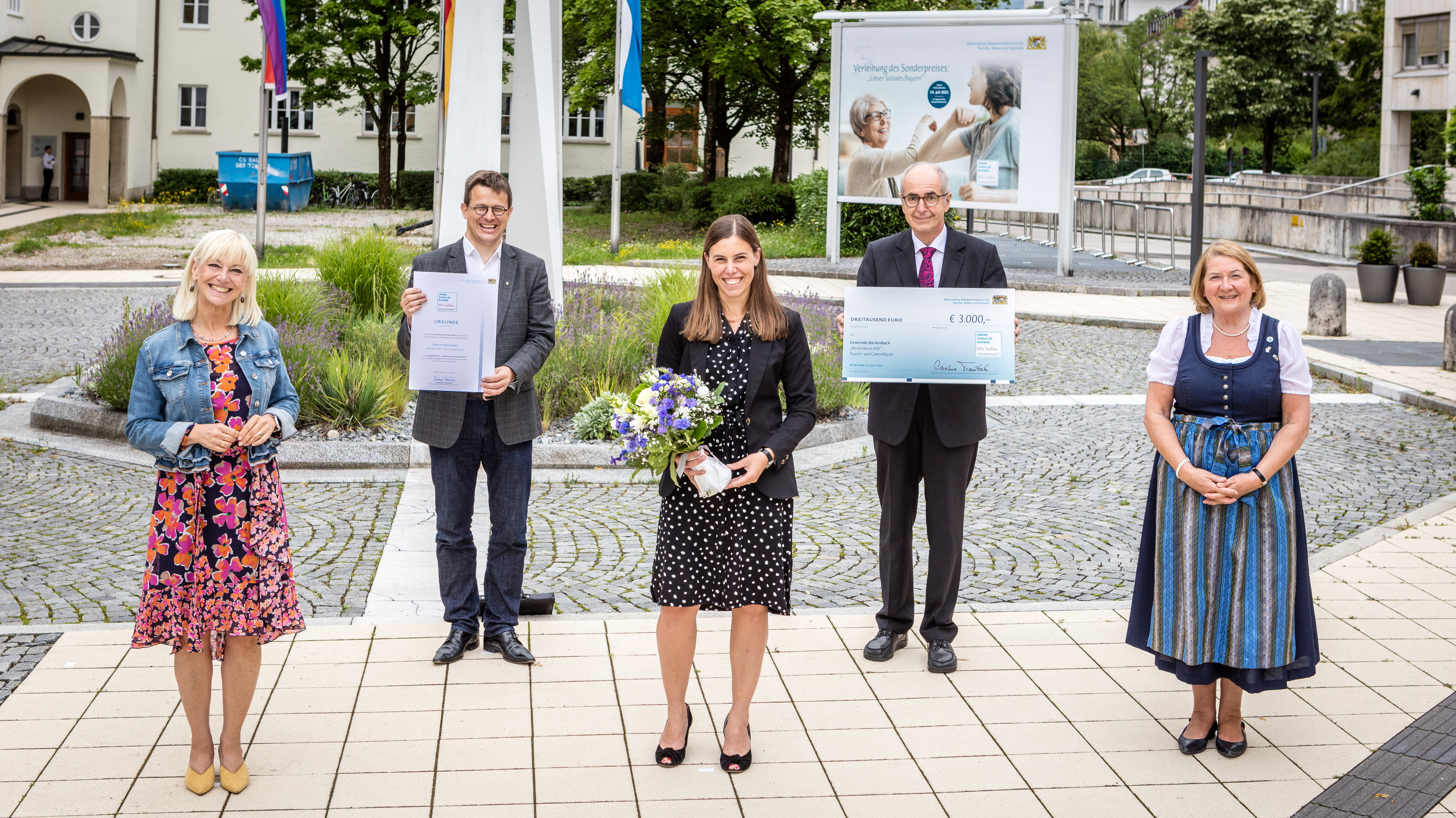 Die ehemalige Staatsministerin Carolina Trautner steht neben vier Preisträgerinnen und Preisträgern des Gewinnerprojekts „Büchenbach hilft“ der Gemeinde Büchenbach. Sie halten eine Urkunde, einen Scheck und einen Blumenstrauß in den Händen.