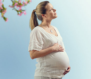 Vergrößerungsansichten für Bild: Foto: Eine schwangere Frau, die ihre Hände schützend auf dem Bauch hält.