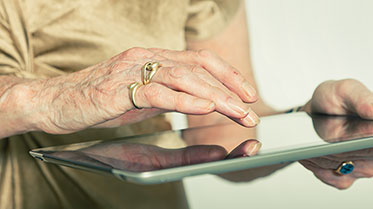 Hand eines älteren Menschen tippt auf Tablet.