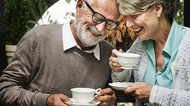 Lachender älterer Mann und lachende ältere Frau mit Kaffeetasse in der Hand.