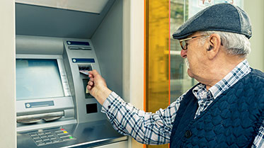 Älterer Mann steckt seine Geldkarte in den Geldautomaten.