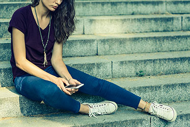 Foto: Eine Jugendliche sitzt auf einer Treppe und tippt eine Nummer in ihr Handy ein 