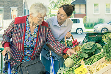 Nahaufnahme: Jüngere Frau hilft älterer Frau mit Gehhilfe beim Einkaufen auf dem Markt.