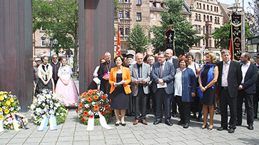 Foto: Gedenktag für die Opfer von Flucht und Vertreibung - Teilnehmer stehen draußen neben Blumenkränzen