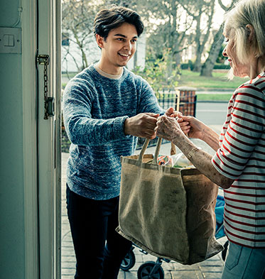 An der Haustür: Junger Mann überreicht Seniorin eine Tasche mit Einkäufen.