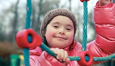 Foto: Junges Mädchen mit Behinderung beim Klettern auf dem Spielplatz.