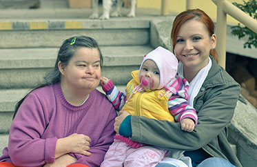 Vergrößerungsansichten für Bild: Frau mit Behinderung zusammen mit einer Frau mit Baby auf dem Arm auf einer Treppe sitzend.