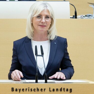 Das Foto zeigt Bayerns Sozialministerin Ulrike Scharf am Rednerpult des bayerischen Landtags stehend.